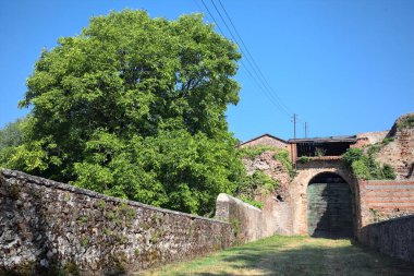 Güneşli bir günde, İtalya 'da terk edilmiş bir sarayın kapısındaki ahşap kapıya uzanan çimlerle kaplı tuğla köprü.