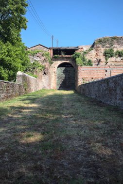 Güneşli bir günde, İtalya 'da terk edilmiş bir sarayın kapısındaki ahşap kapıya uzanan çimlerle kaplı tuğla köprü.