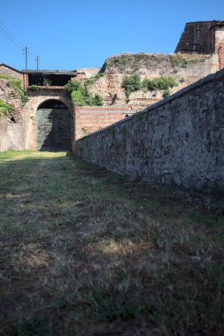 Güneşli bir günde, İtalya 'da terk edilmiş bir sarayın kapısındaki ahşap kapıya uzanan çimlerle kaplı tuğla köprü.