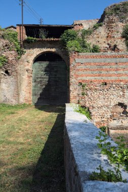 Güneşli bir günde, İtalya 'da terk edilmiş bir sarayın kapısındaki ahşap kapıya uzanan çimlerle kaplı tuğla köprü.