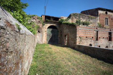 Güneşli bir günde, İtalya 'da terk edilmiş bir sarayın kapısındaki ahşap kapıya uzanan çimlerle kaplı tuğla köprü.