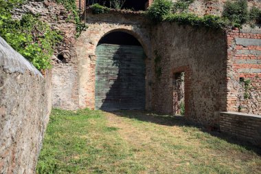 Güneşli bir günde, İtalya 'da terk edilmiş bir sarayın kapısındaki ahşap kapıya uzanan çimlerle kaplı tuğla köprü.