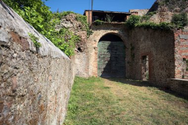 Güneşli bir günde, İtalya 'da terk edilmiş bir sarayın kapısındaki ahşap kapıya uzanan çimlerle kaplı tuğla köprü.