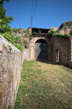 Güneşli bir günde, İtalya 'da terk edilmiş bir sarayın kapısındaki ahşap kapıya uzanan çimlerle kaplı tuğla köprü.