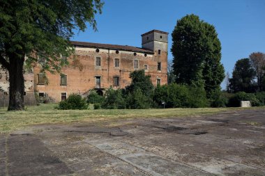 Kenarında kavak ağacı olan bir meydan ve arka planında ağaçlarla çevrili terk edilmiş bir saray İtalya kırsalında güneşli bir günde