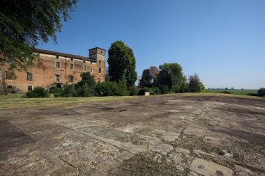 Kenarında kavak ağacı olan bir meydan ve arka planında ağaçlarla çevrili terk edilmiş bir saray İtalya kırsalında güneşli bir günde