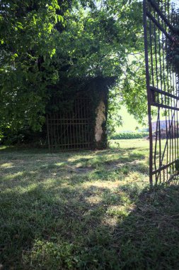 Ağaçlarla çevrili gölgede bir sınır duvarının açık kapısı