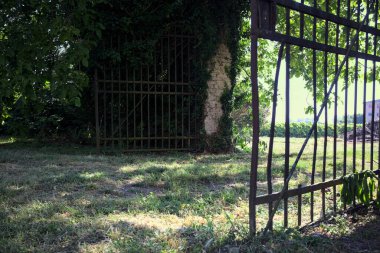 Ağaçlarla çevrili gölgede bir sınır duvarının açık kapısı