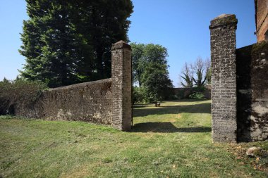 Bir şatonun kenarındaki patika, uzaktaki bir köprünün kemerlerinin altından geçiyor, yere düşen ağaçların gölgeleriyle.