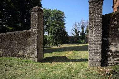 Bir şatonun kenarındaki patika, uzaktaki bir köprünün kemerlerinin altından geçiyor, yere düşen ağaçların gölgeleriyle.