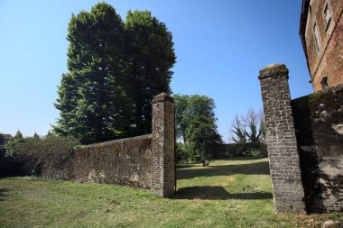 Bir şatonun kenarındaki patika, uzaktaki bir köprünün kemerlerinin altından geçiyor, yere düşen ağaçların gölgeleriyle.