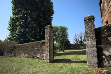 Bir şatonun kenarındaki patika, uzaktaki bir köprünün kemerlerinin altından geçiyor, yere düşen ağaçların gölgeleriyle.
