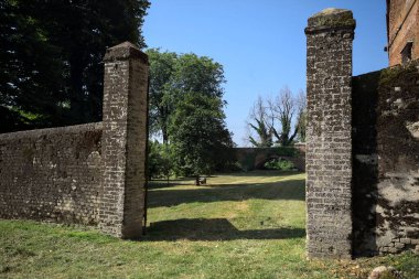Bir şatonun kenarındaki patika, uzaktaki bir köprünün kemerlerinin altından geçiyor, yere düşen ağaçların gölgeleriyle.