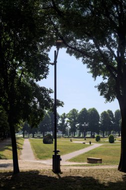 Bir köşeden görünen ve ağaçların ve bankların siluetleriyle çerçevelenmiş kavak ağaçlarıyla çevrili bir meydan.