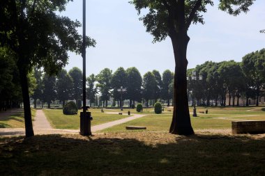 Bir köşeden görünen ve ağaçların ve bankların siluetleriyle çerçevelenmiş kavak ağaçlarıyla çevrili bir meydan.