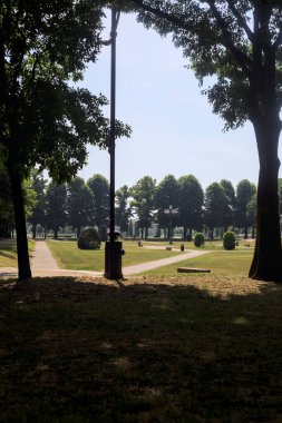 Bir köşeden görünen ve ağaçların ve bankların siluetleriyle çerçevelenmiş kavak ağaçlarıyla çevrili bir meydan.