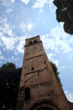 Arka plan olarak kısmen bulutlu bir gökyüzü olan ağaçların yanındaki tuğla çan kulesinin kalıntıları.