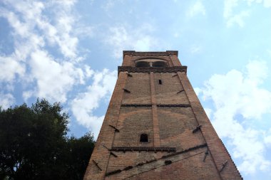 Arka plan olarak kısmen bulutlu bir gökyüzü olan ağaçların yanındaki tuğla çan kulesinin kalıntıları.