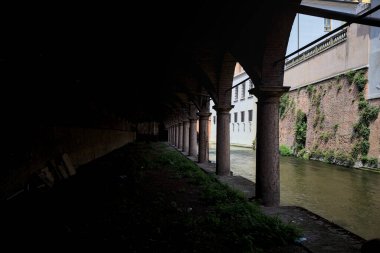Gölgede sütunlar, İtalyan kasabasının duvarlarıyla çevrili bir su deresinin yanında kemerler.