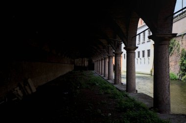 Gölgede sütunlar, İtalyan kasabasının duvarlarıyla çevrili bir su deresinin yanında kemerler.