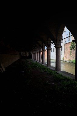 Gölgede sütunlar, İtalyan kasabasının duvarlarıyla çevrili bir su deresinin yanında kemerler.