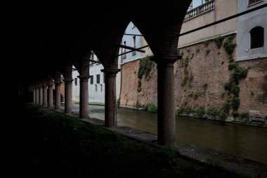 Gölgede sütunlar, İtalyan kasabasının duvarlarıyla çevrili bir su deresinin yanında kemerler.