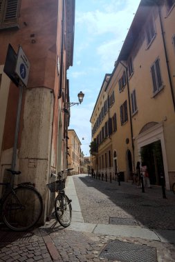 Güneşli bir günde İtalya 'da bir binanın köşesine parketmiş bisikletli dar kaldırımlı cadde.