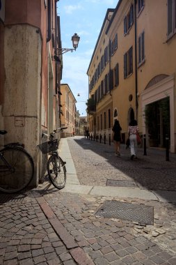 Güneşli bir günde İtalya 'da bir binanın köşesine parketmiş bisikletli dar kaldırımlı cadde.