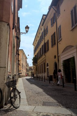 Güneşli bir günde İtalya 'da bir binanın köşesine parketmiş bisikletli dar kaldırımlı cadde.