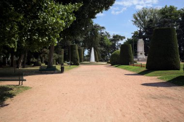 Ağaçlarla çevrili patika ve bitkilerle çevrili. Parkta bir çeşme var.