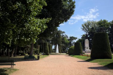 Ağaçlarla çevrili patika ve bitkilerle çevrili. Parkta bir çeşme var.