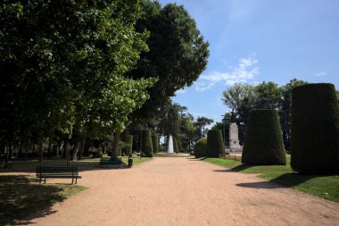 Ağaçlarla çevrili patika ve bitkilerle çevrili. Parkta bir çeşme var.