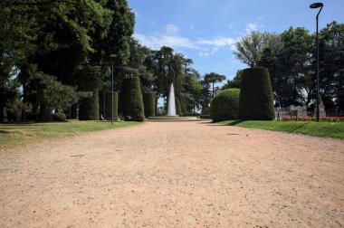 Ağaçlarla çevrili patika ve bitkilerle çevrili. Parkta bir çeşme var.