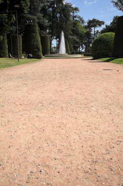 Ağaçlarla çevrili patika ve bitkilerle çevrili. Parkta bir çeşme var.