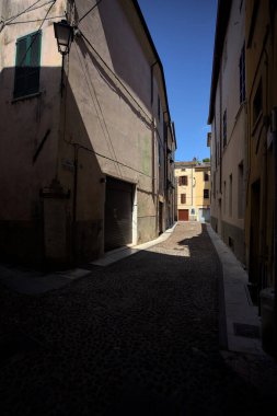 Kavisli dar bir sokak. Köşeden görünen bir gölge tarafından ikiye bölünmüş.