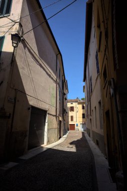 Kavisli dar bir sokak. Köşeden görünen bir gölge tarafından ikiye bölünmüş.