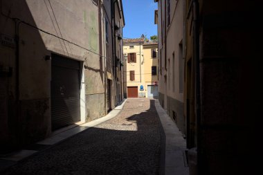 Kavisli dar bir sokak. Köşeden görünen bir gölge tarafından ikiye bölünmüş.