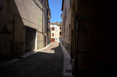 Kavisli dar bir sokak. Köşeden görünen bir gölge tarafından ikiye bölünmüş.