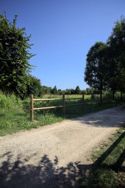 Yol ve ahşap korkuluklar, güneşli bir günde bir parktaki çayırın yanındaki su deresinin üzerinde.