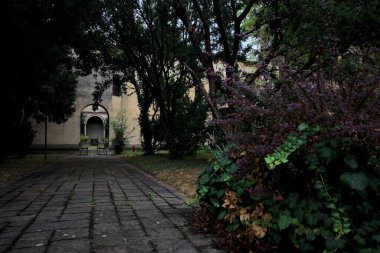 Bahçenin ağaçlarıyla çevrili bir yoldan görünen bir sarayın verandası ve kemer yolu.