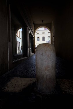 Mağaza pencereleri ve başlangıcında bir direği olan gölgede kemerli bir yol.