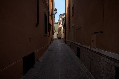 Üzerinde açık bir gökyüzü olan gölgede dar dar bir ara sokak.