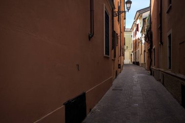 Üzerinde açık bir gökyüzü olan gölgede dar dar bir ara sokak.