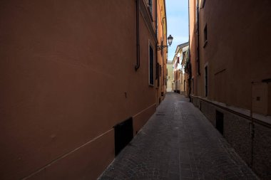 Üzerinde açık bir gökyüzü olan gölgede dar dar bir ara sokak.