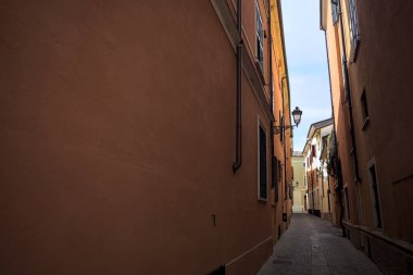 Üzerinde açık bir gökyüzü olan gölgede dar dar bir ara sokak.