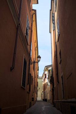 Üzerinde açık bir gökyüzü olan gölgede dar dar bir ara sokak.