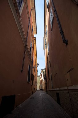 Üzerinde açık bir gökyüzü olan gölgede dar dar bir ara sokak.