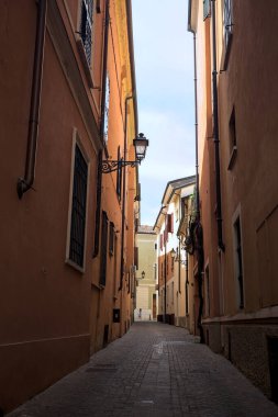 Üzerinde açık bir gökyüzü olan gölgede dar dar bir ara sokak.