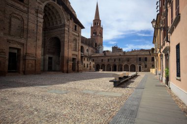 Mantova, İtalya - 27 Temmuz 2025 - Güneşli bir günde San Andrea Bazilikası 'nın bir tarafında çan kulesi ve bitişik binası ile kaldırımlı meydan