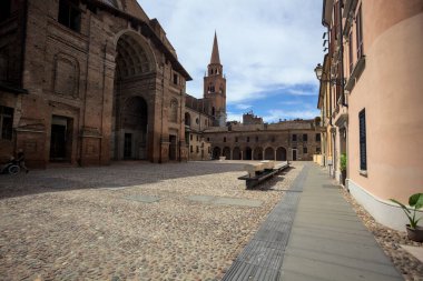 Mantova, İtalya - 27 Temmuz 2025 - Güneşli bir günde San Andrea Bazilikası 'nın bir tarafında çan kulesi ve bitişik binası ile kaldırımlı meydan
